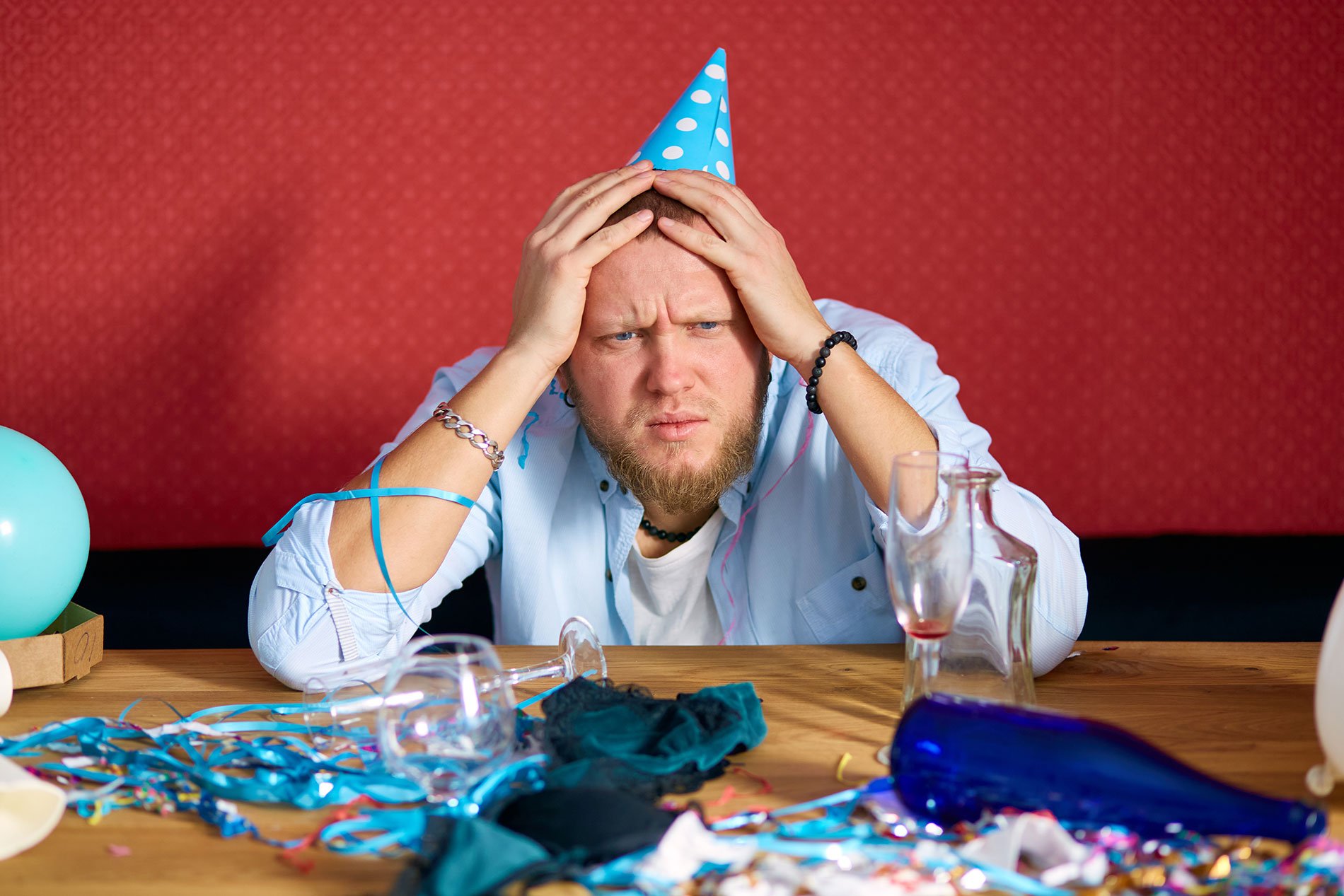 Ein Mann leidet nach einer Feier an einem Kater: Kopfschmerzen und Übelkeit sind häufige Symptome.